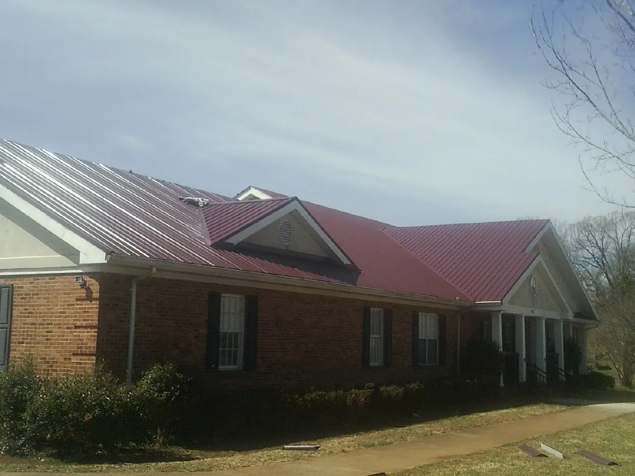 Red metal roof with gabled entries on a long brick building, from a Hail Damage Roof Repair job in Pine Bush