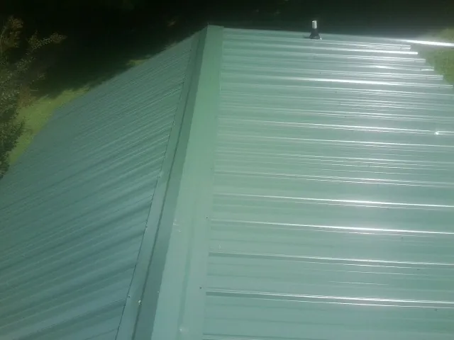 New green metal panels meeting at the ridge of a roof — Flat Roof Repair work by our crew in Pine Bush