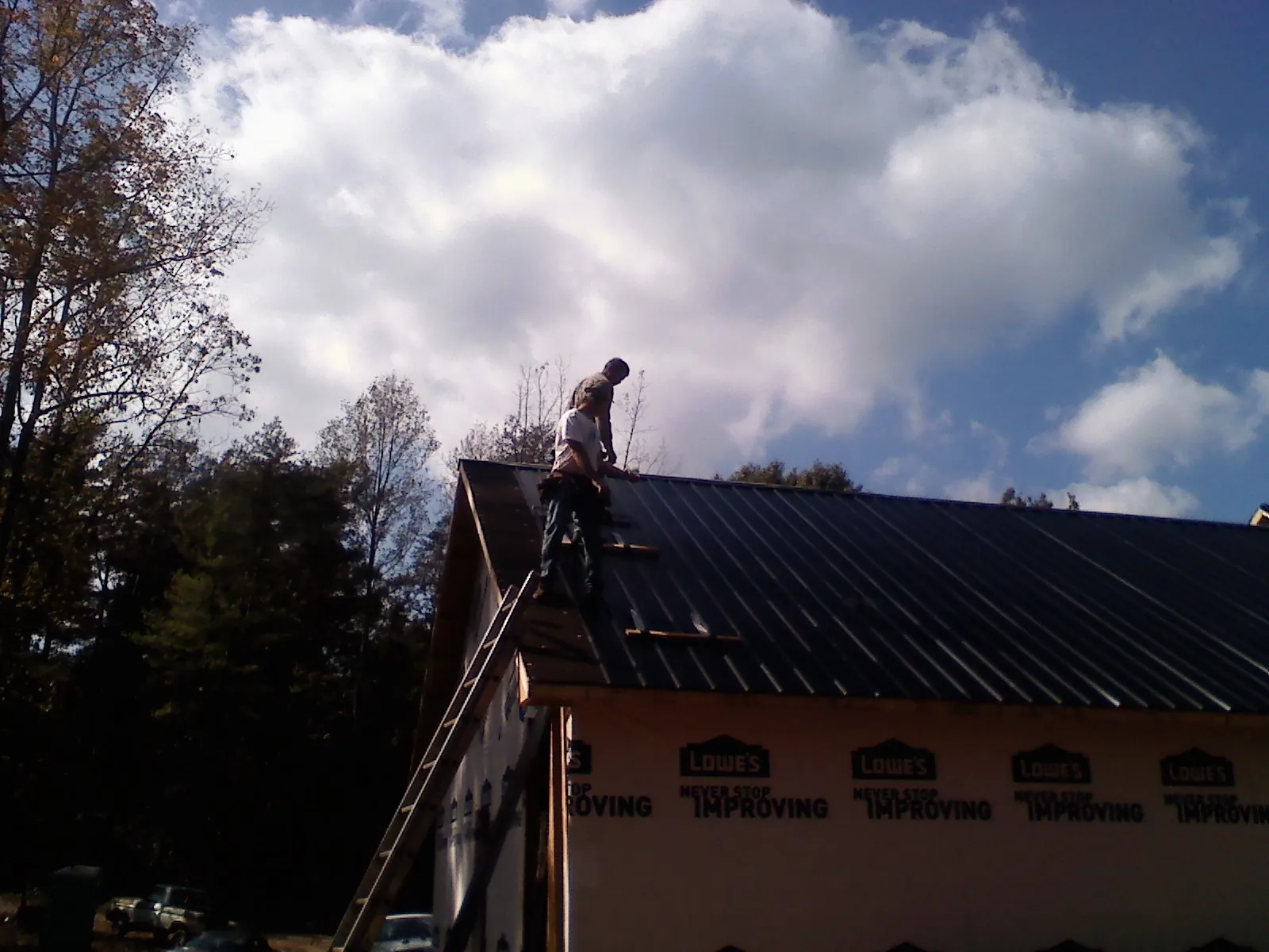 Roofer fastening dark metal panels high against a cloudy sky, from a Roof Inspection job in Pine Bush