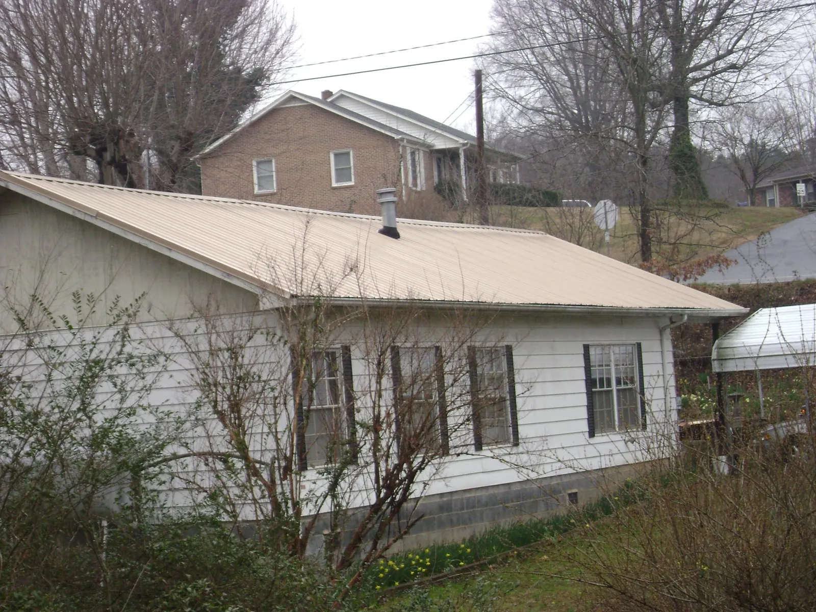 Tan metal roof on a white sided house set into a hillside — Commercial Roofing by Roofing Brothers in Pine Bush